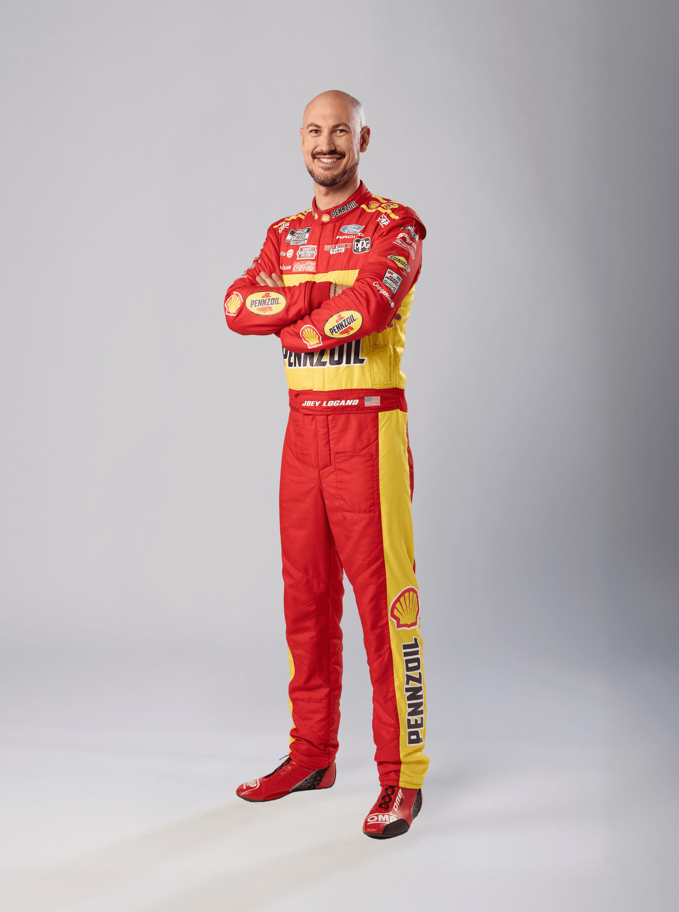 Smiling driver with arms folded in a red and yellow Shell Pennzoil suit and matching boots