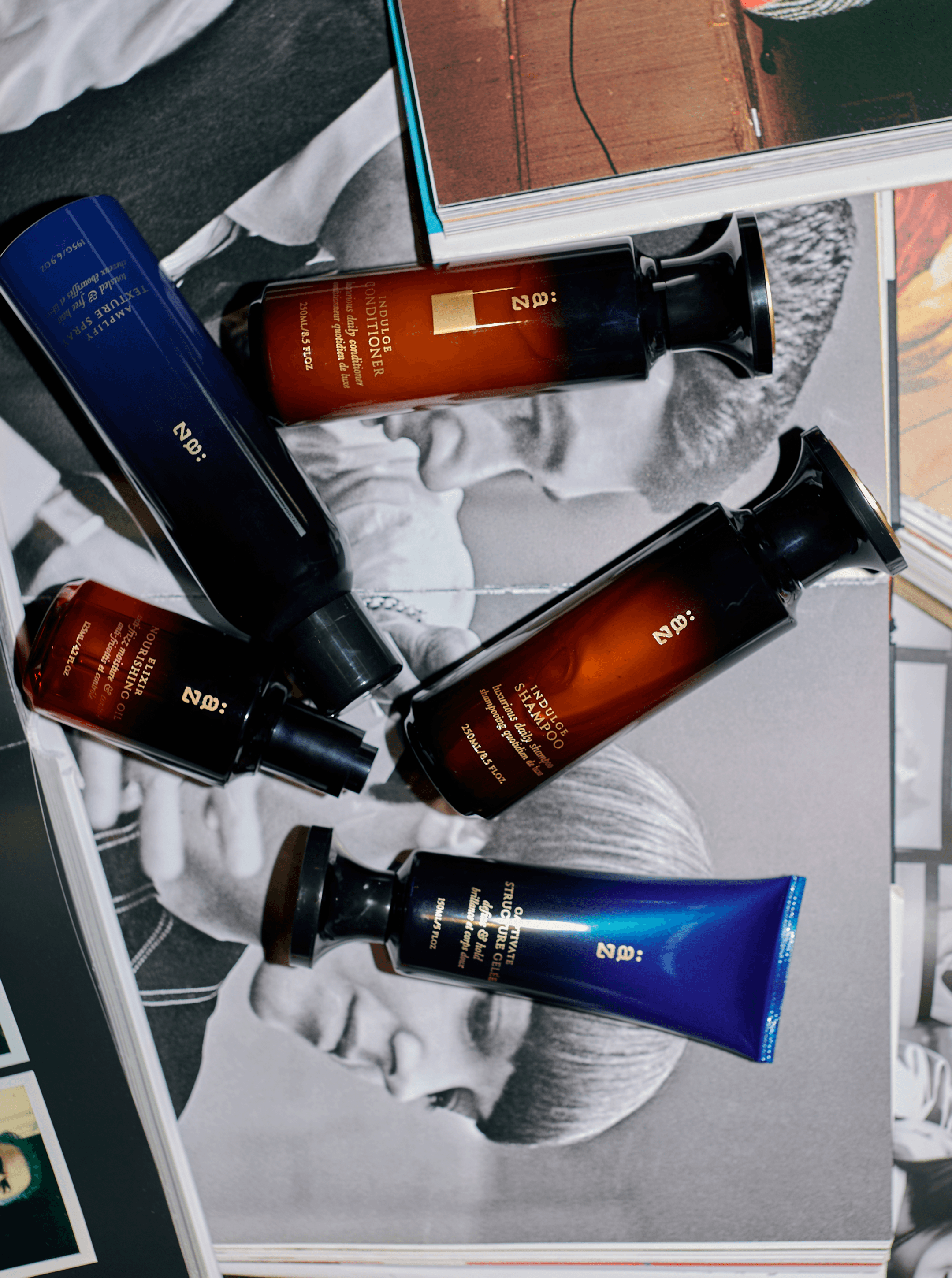 Five AZ bottles and a blue gelee tube arranged over black-and-white portrait spreads on a table