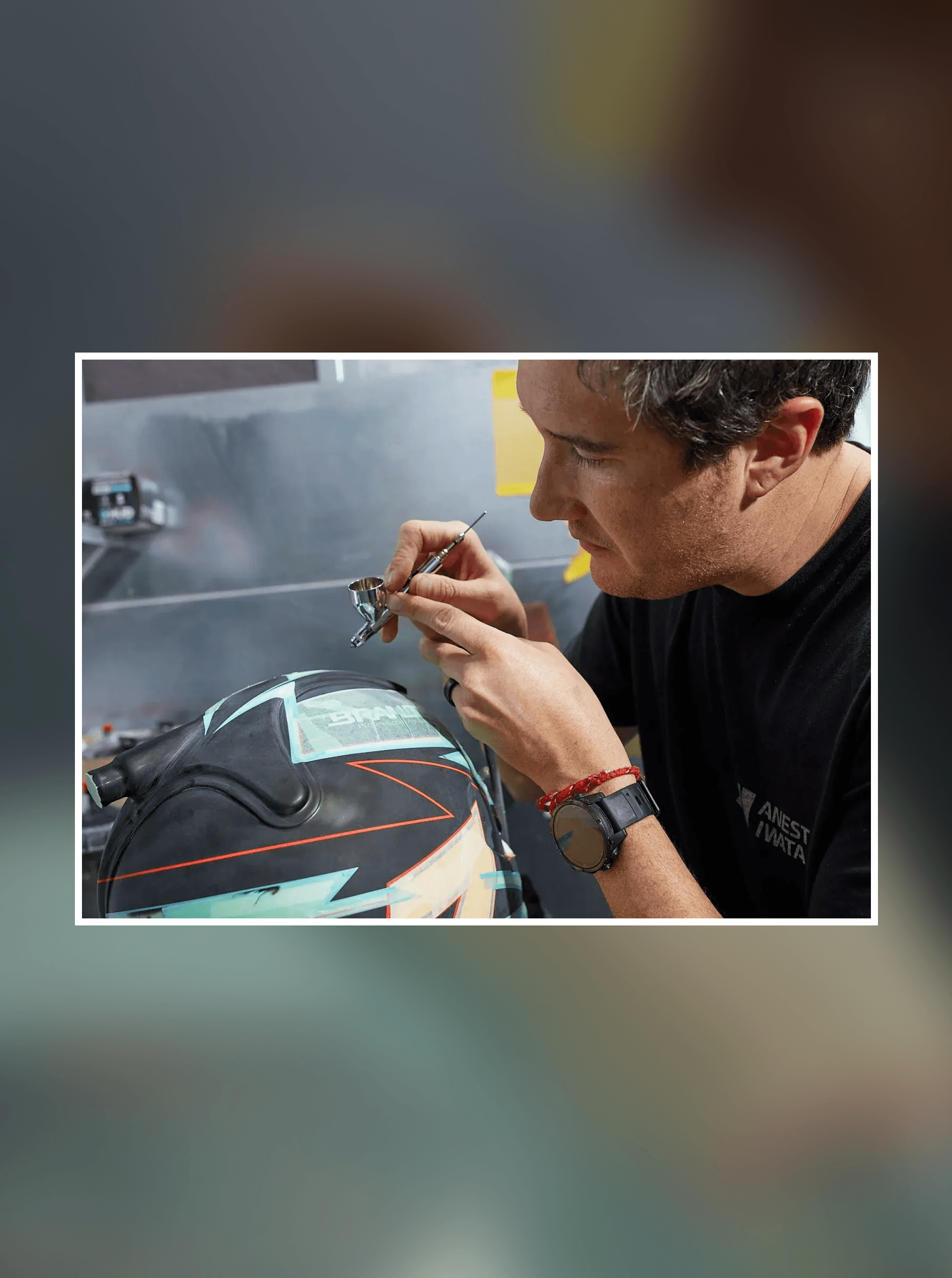 Painter leaning in with a fine brush to detail a black helmet striped in teal and orange