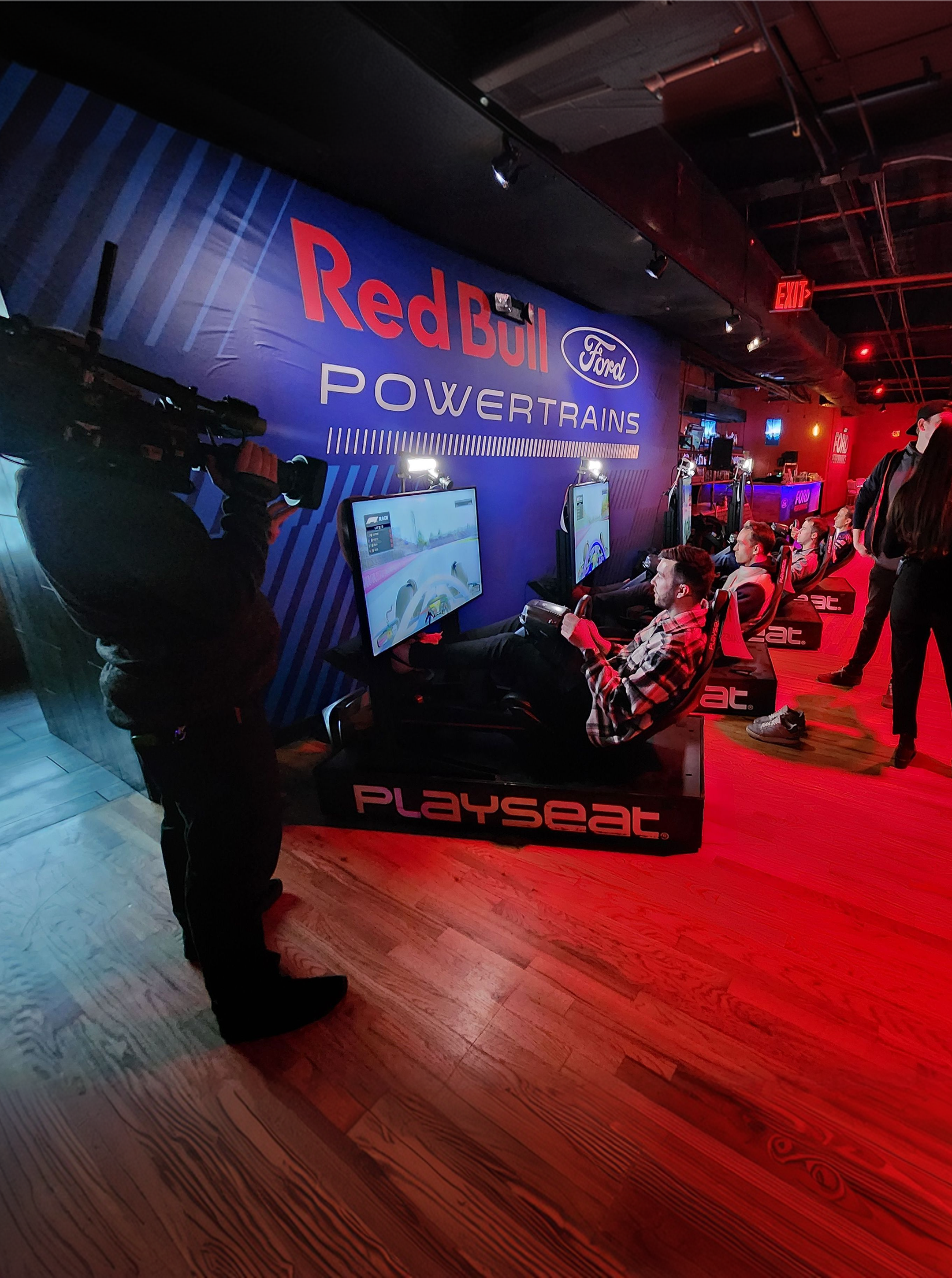 Camera operator filming a man in a Playseat racing simulator against a Red Bull Ford Powertrains backdrop
