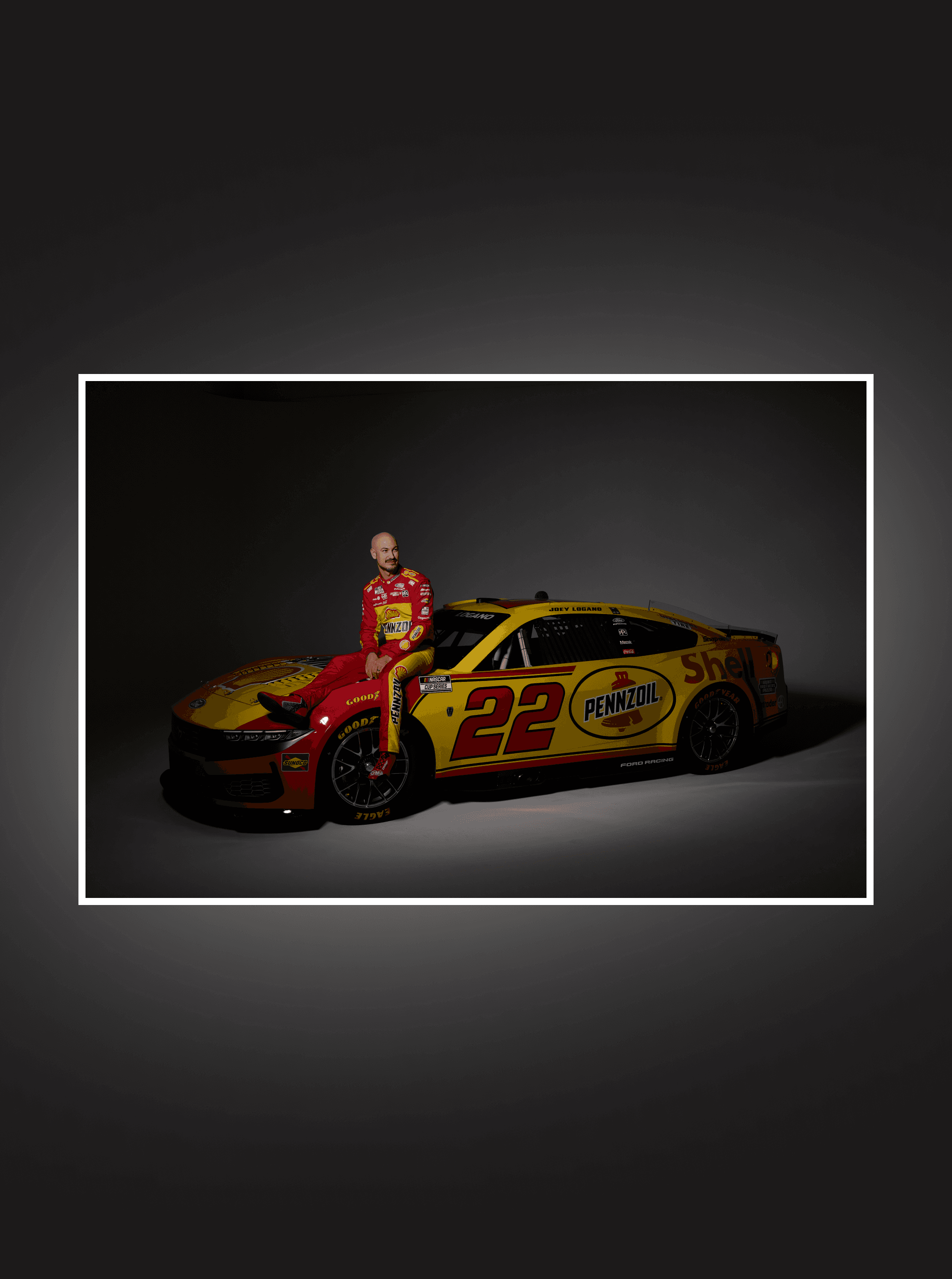 Driver perched on the hood of the number 22 Shell Pennzoil Cup car against a gray studio backdrop