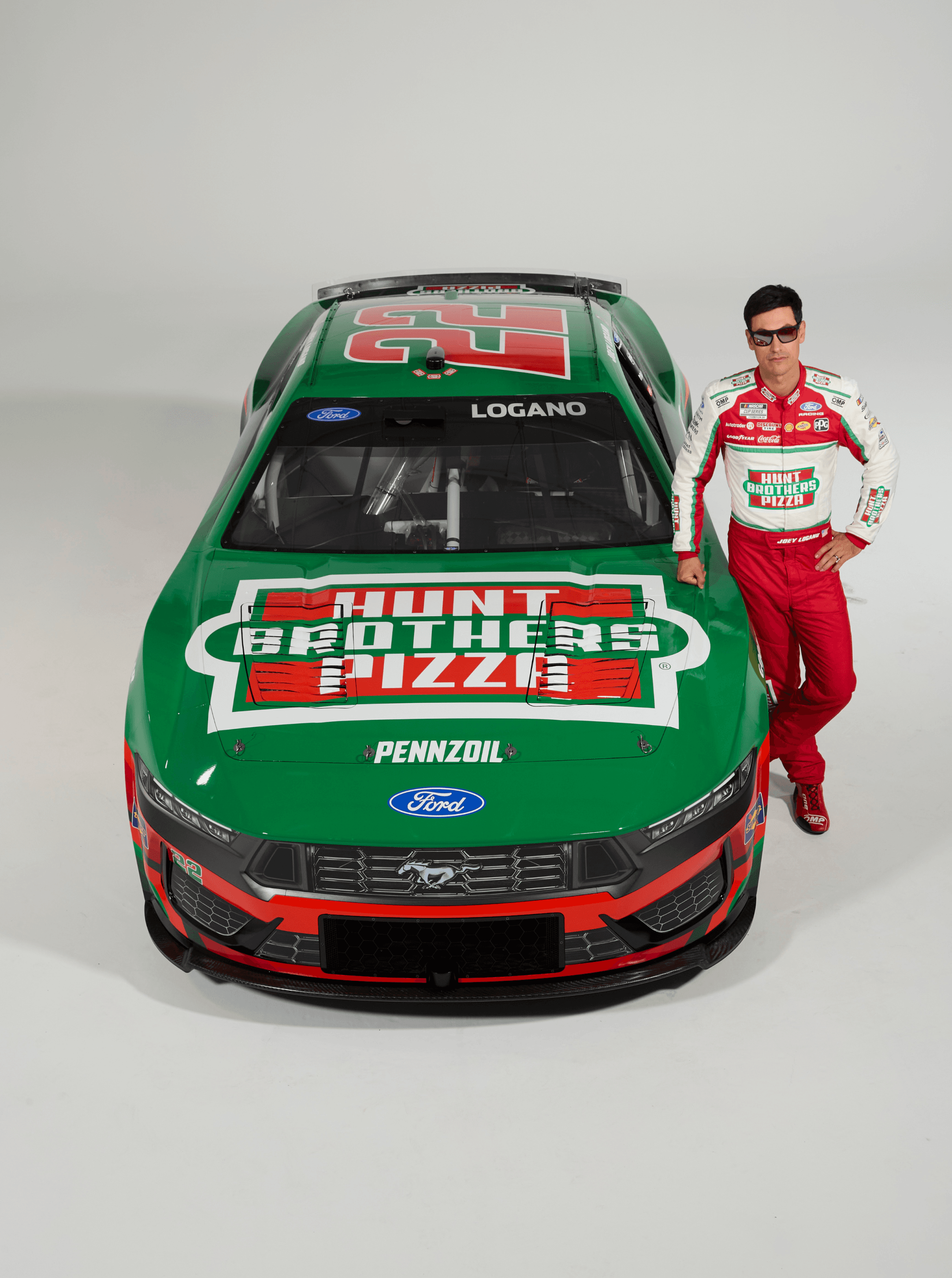 Driver in sunglasses posed beside the front fender of the green number 22 car, Pennzoil decal on the hood