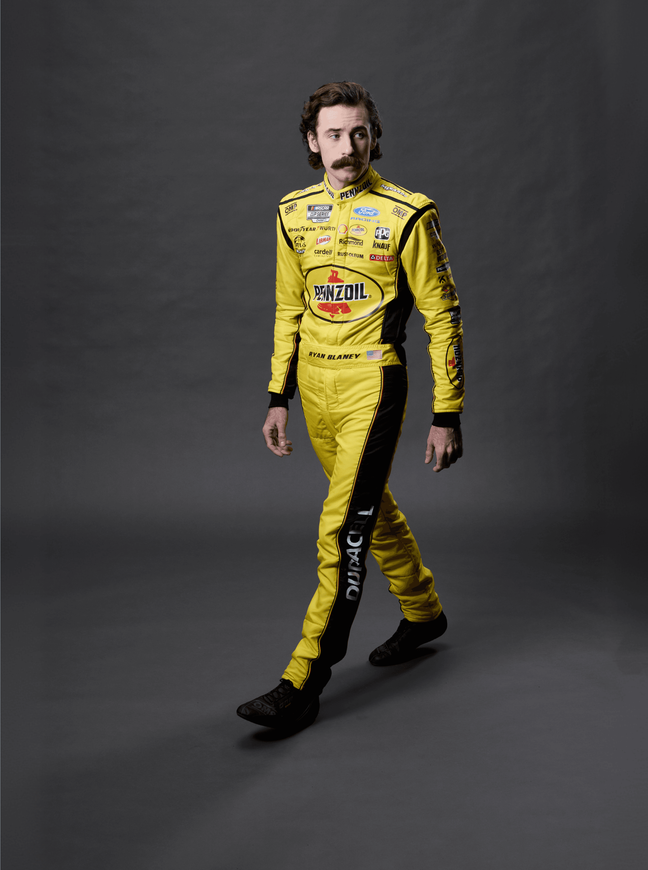 Full-length studio shot of a driver mid-stride in a yellow Pennzoil suit with Duracell down the leg
