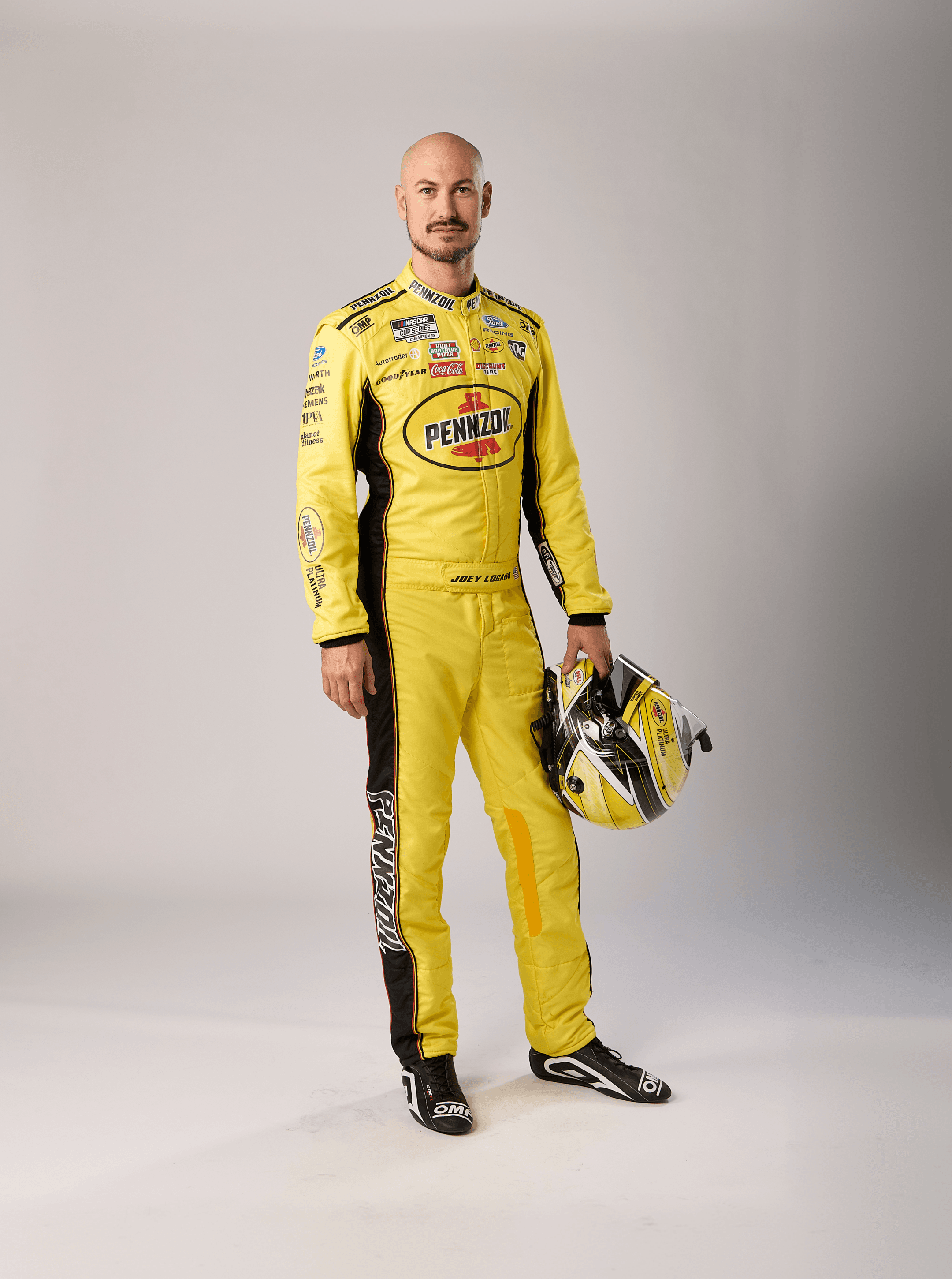 Driver standing still in a yellow Pennzoil suit, black and yellow helmet resting against his hip