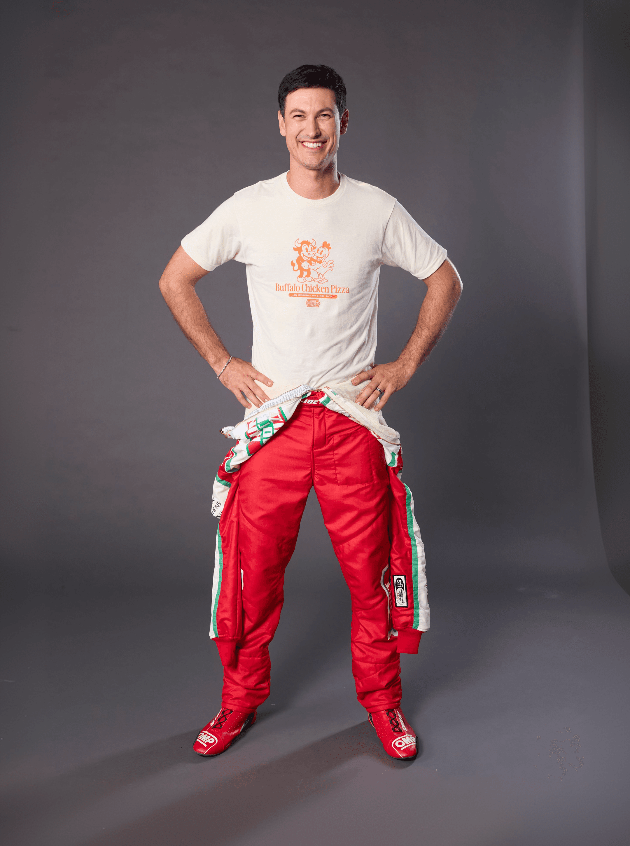 Full length shot of the driver with his fire suit tied at the waist over a Buffalo Chicken Pizza tee