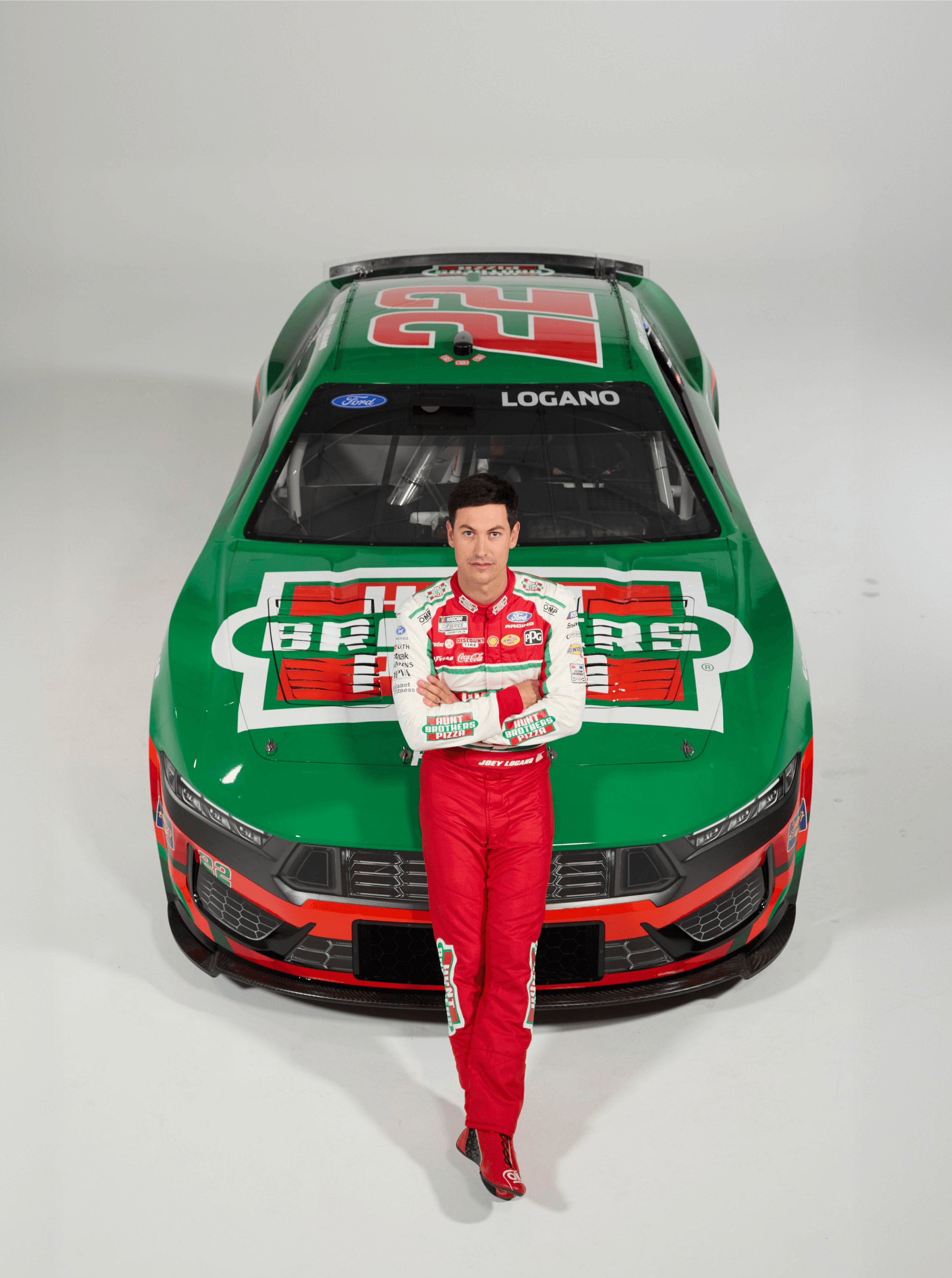 Driver leaning back against the nose of the green Hunt Brothers Pizza race car with arms folded