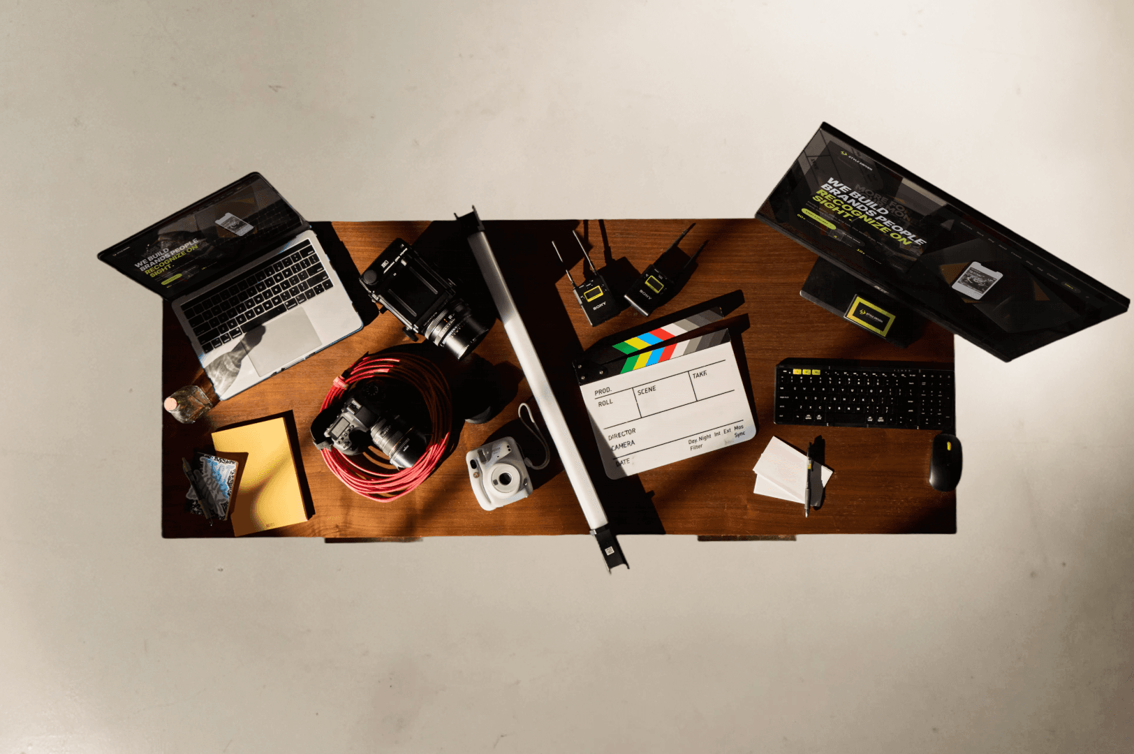 Style Driven creative tools laid out on a walnut desk — laptop, cinema camera, clapperboard, audio gear, monitor